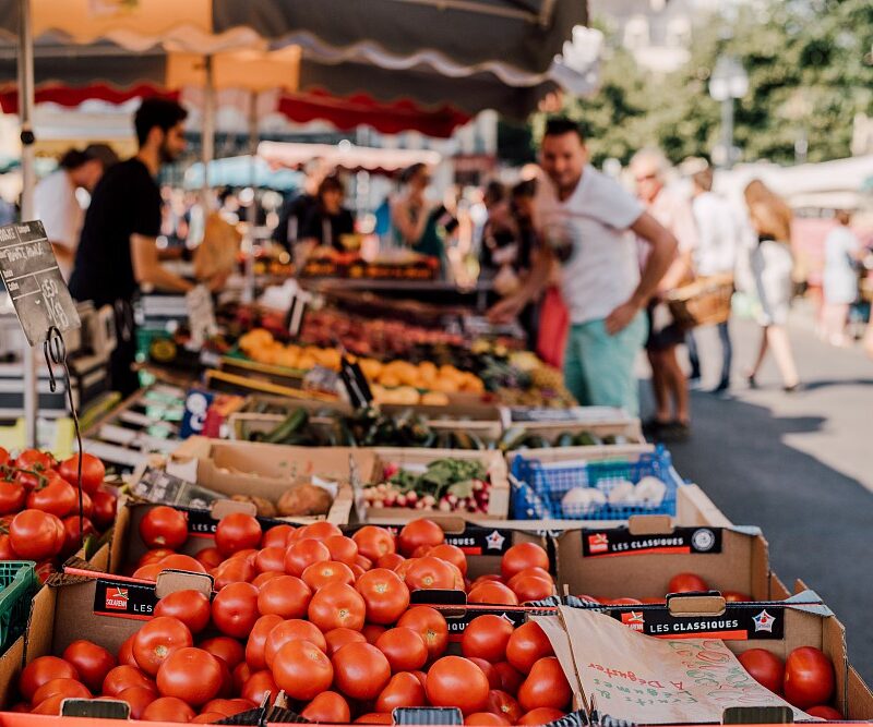 Des personnes flânant entre les étals colorés d’un marché breton, découvrant produits locaux, fruits de mer, légumes frais et spécialités artisanales dans une ambiance conviviale.