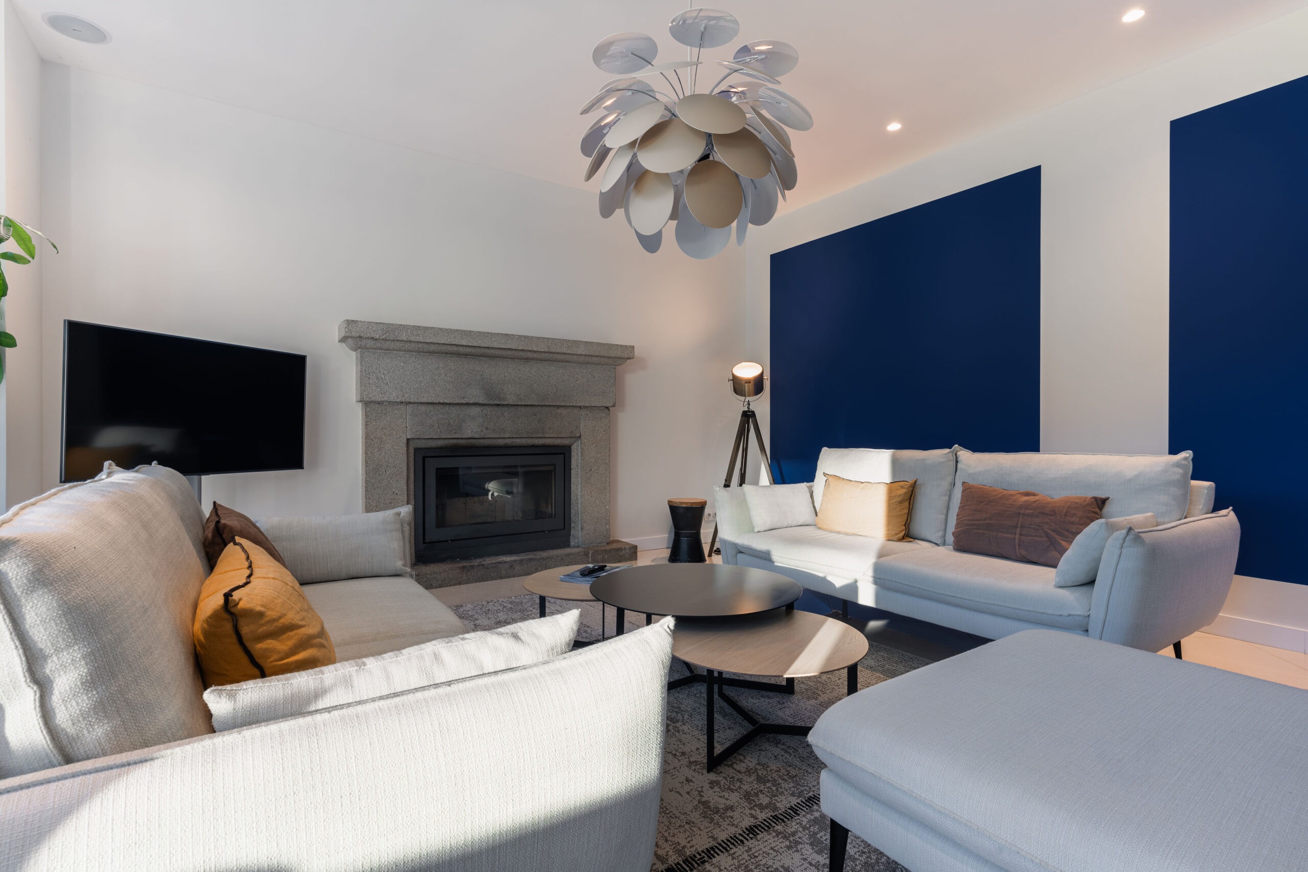Salon lumineux et moderne d'un appartement de location saisonnière au Domaine de Stang Bihan, Concarneau. Canapés gris clair, cheminée en pierre, grand écran plat et luminaire design. Ambiance chaleureuse et relaxante.