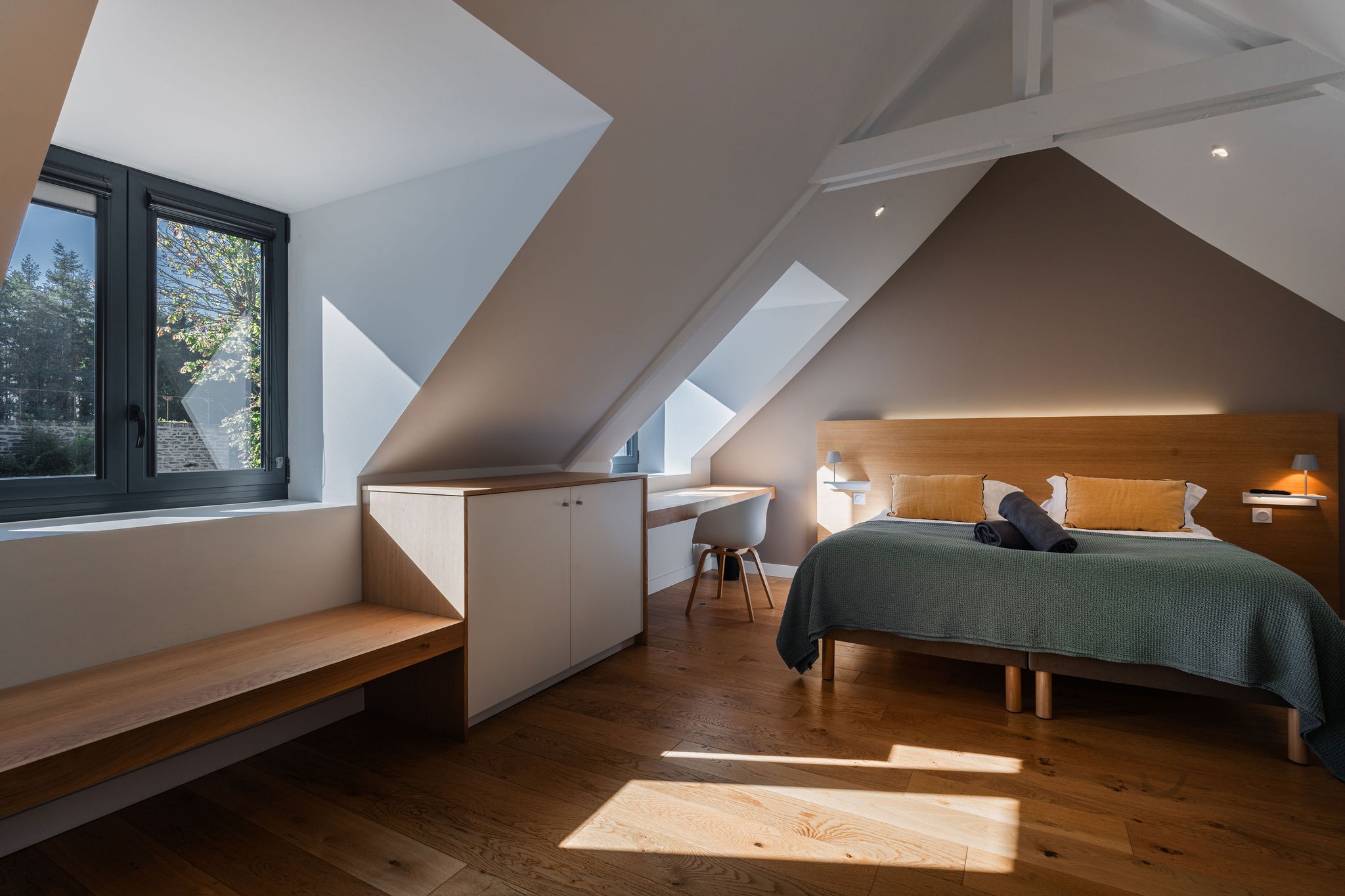 Chambre design dans Le Recouvrance à Concarneau, avec lit double, mobilier en bois clair, lumière naturelle abondante et vue sur les arbres du Domaine de Stang Bihan.