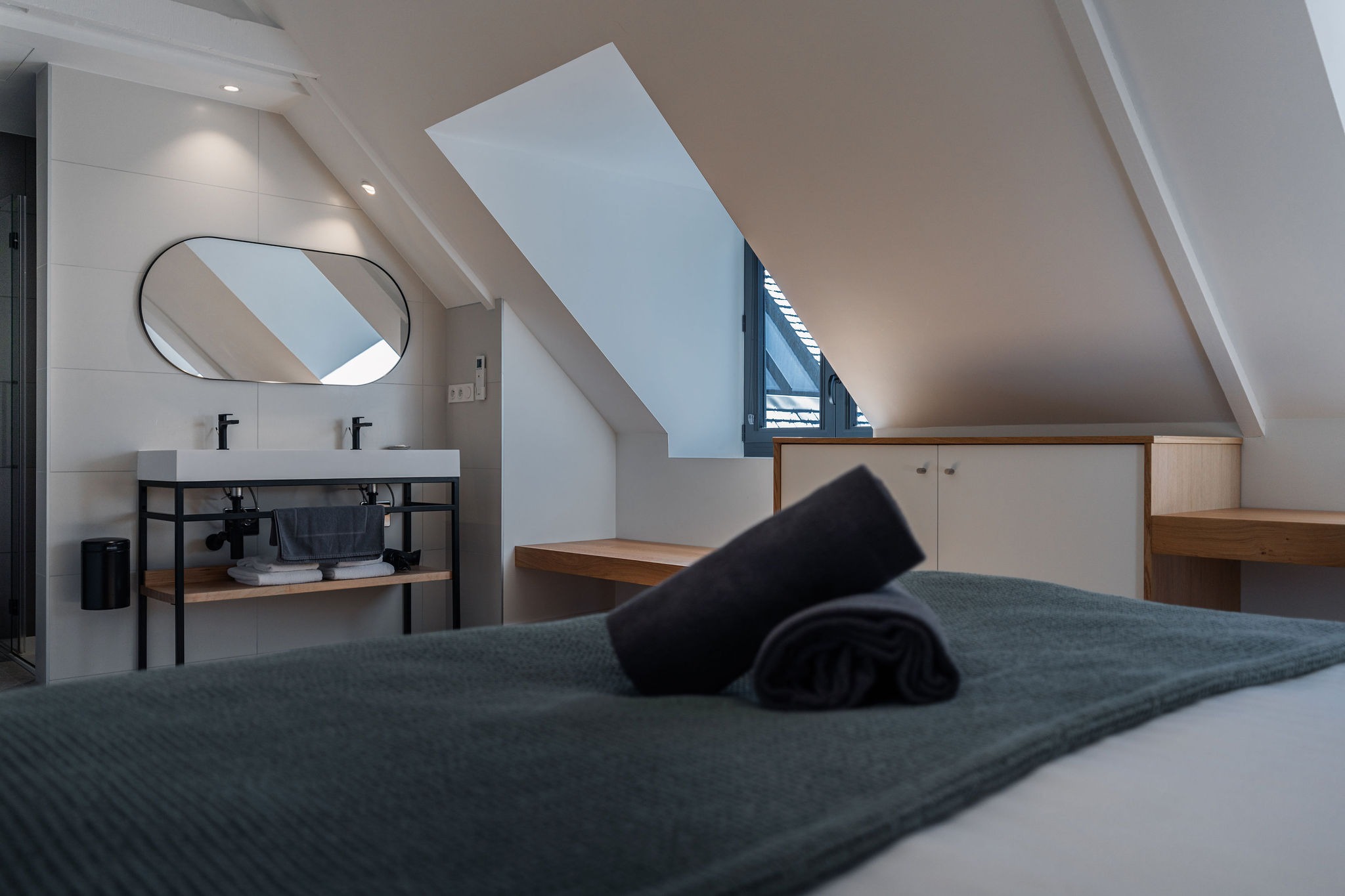 Salle de bain contemporaine attenante à la chambre du logement Le Recouvrance, avec double vasque, serviettes et lumière naturelle dans un espace mansardé au Domaine de Stang Bihan à Concarneau.