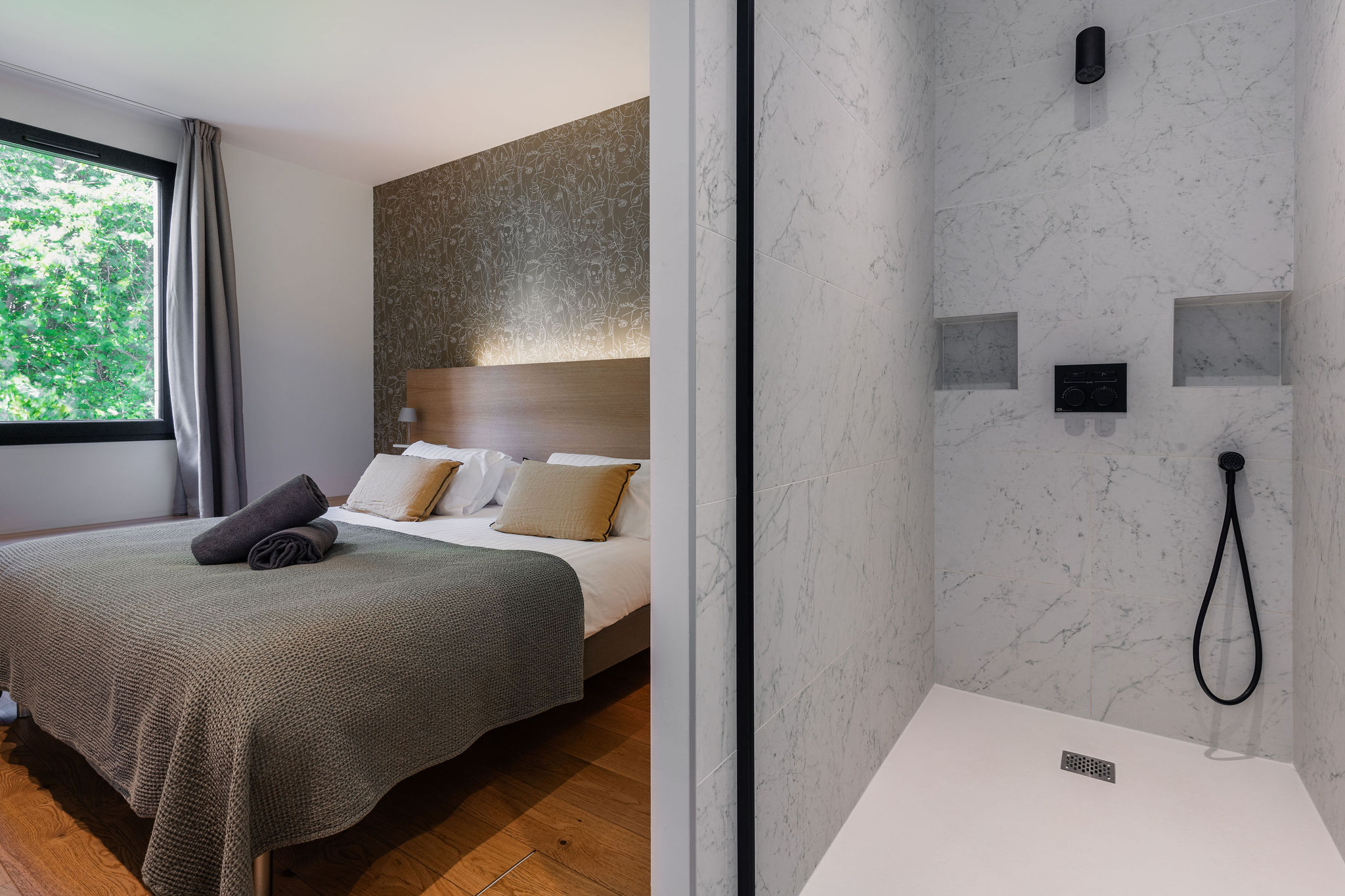 Chambre confortable de Le Corentin avec grande fenêtre donnant sur la nature et douche moderne en marbre blanc, dans un cadre haut de gamme avec vue mer sur les Glénan.