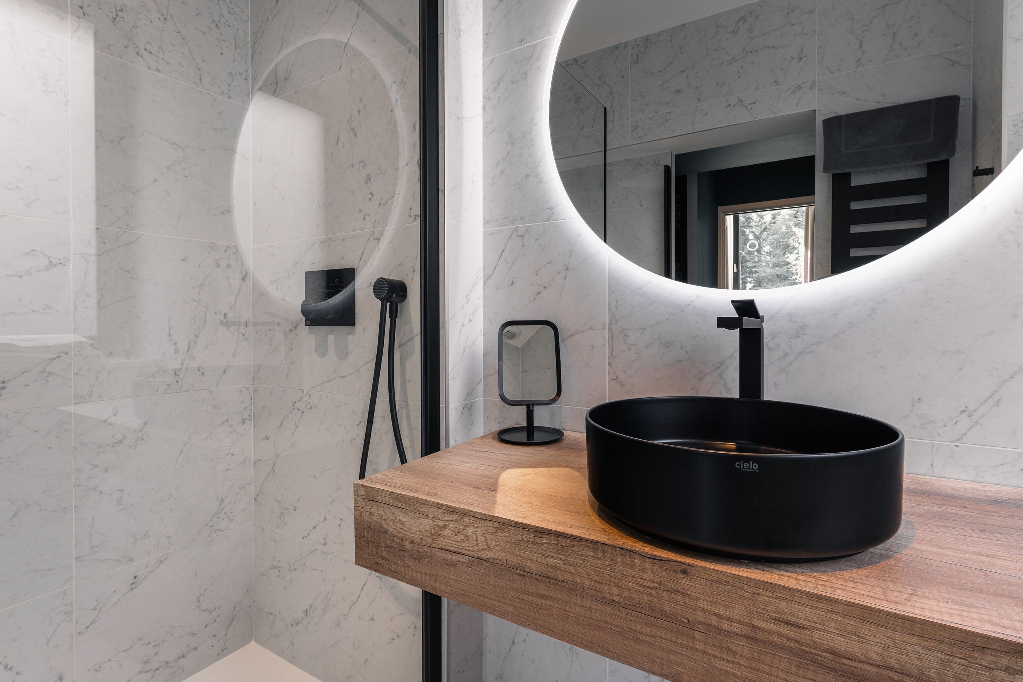 Salle de bain moderne du logement Marche Avec avec vasque noire, miroir rond rétroéclairé, douche à l’italienne et robinetterie noire au Domaine de Stang Bihan à Concarneau