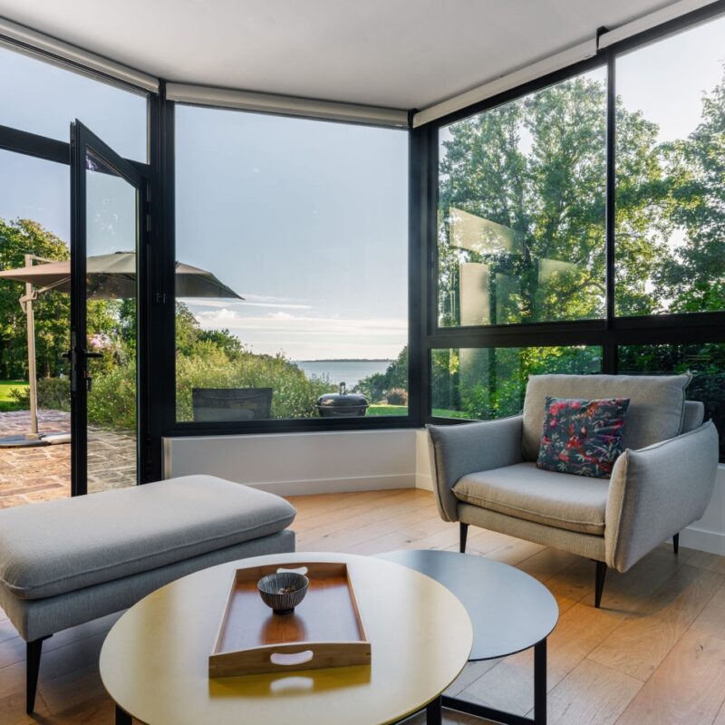 Salon moderne de l'appartement Le Corentin avec larges baies vitrées donnant sur une terrasse, vue mer panoramique à 180° sur les Glénan, dans le domaine de Stang Bihan à Concarneau.