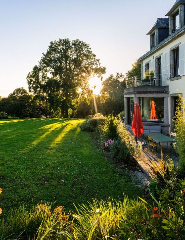 Maison du Domaine de Stang Bihan à Concarneau avec jardin arboré et vue sur la mer au coucher du soleil.