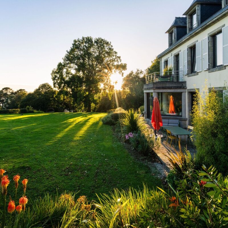 Maison du Domaine de Stang Bihan à Concarneau avec jardin arboré et vue sur la mer au coucher du soleil.