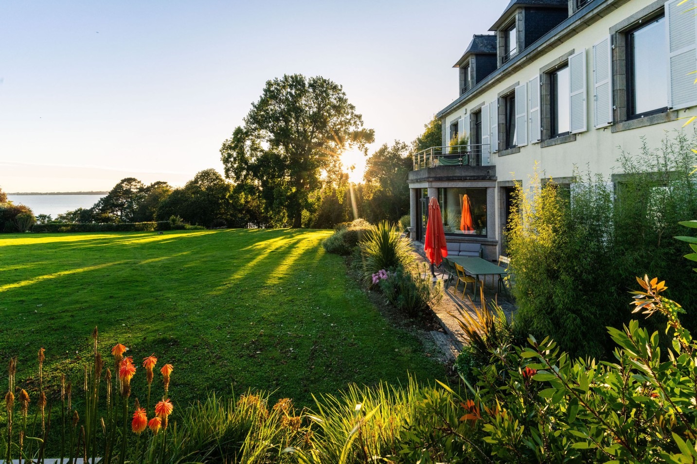 Maison du Domaine de Stang Bihan à Concarneau avec jardin arboré et vue sur la mer au coucher du soleil.