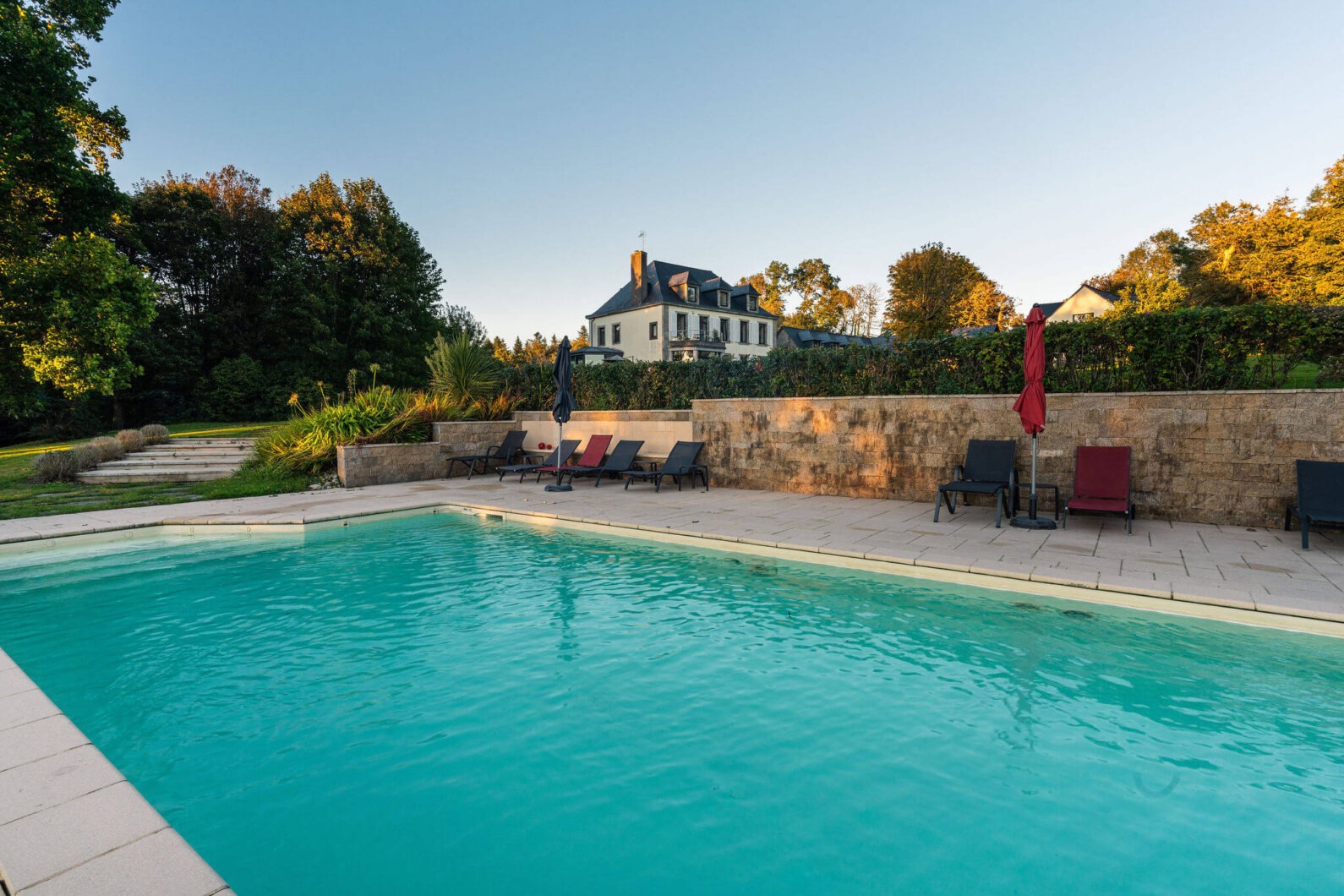 Piscine extérieure avec transats au Domaine de Stang Bihan, vue sur la maison principale entourée de verdure à Concarneau.