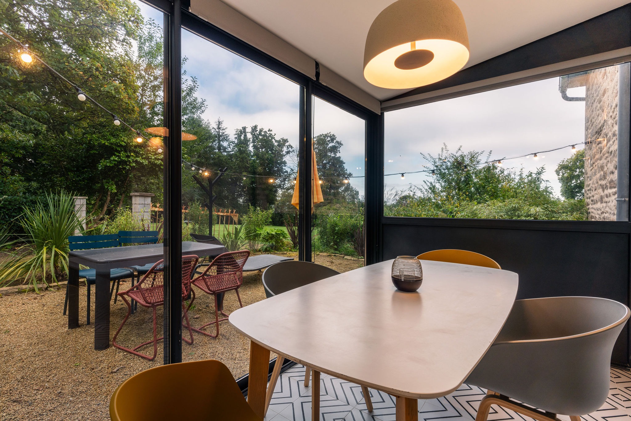 Salle à manger en véranda du logement le Sant C’hireg au Domaine de Stang Bihan, avec table intérieure et coin repas extérieur dans un jardin arboré