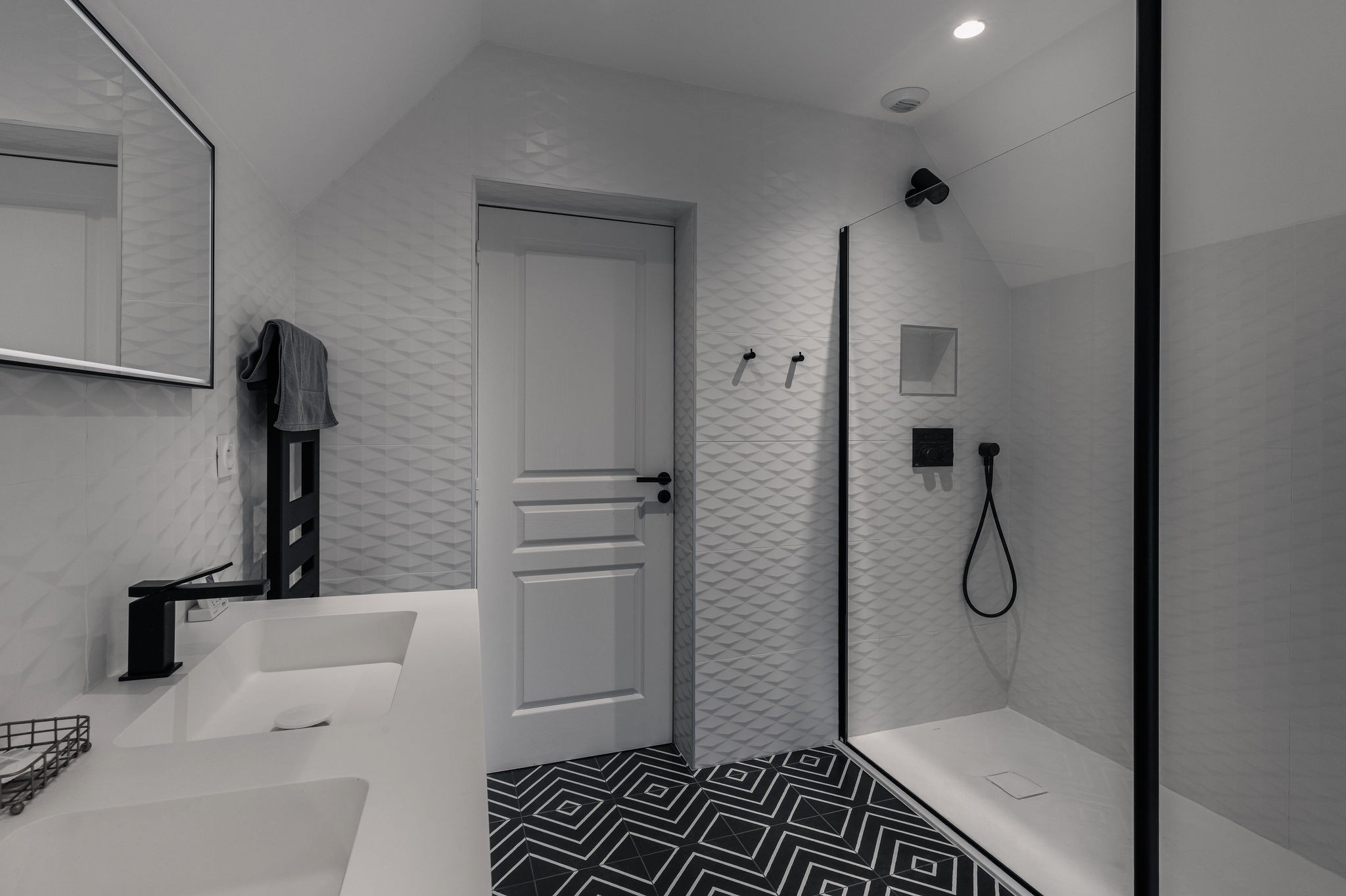 Salle de bain moderne avec double vasque, douche à l’italienne, robinetterie noire et carrelage graphique – Domaine de Stang Bihan à Concarneau