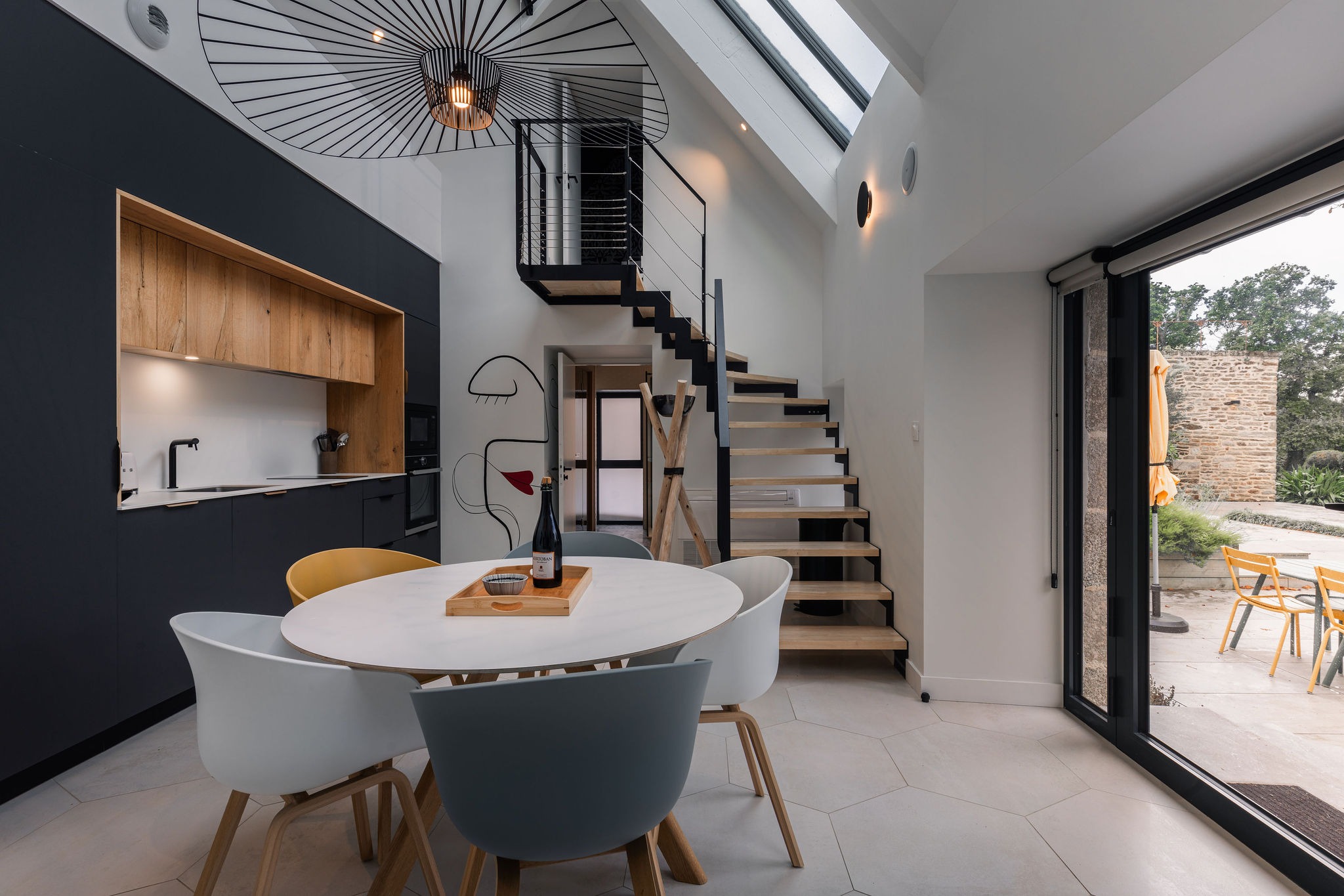 Séjour lumineux du gîte L’Étoile du Roy avec coin repas, cuisine design et escalier vers l'étage, sous une verrière