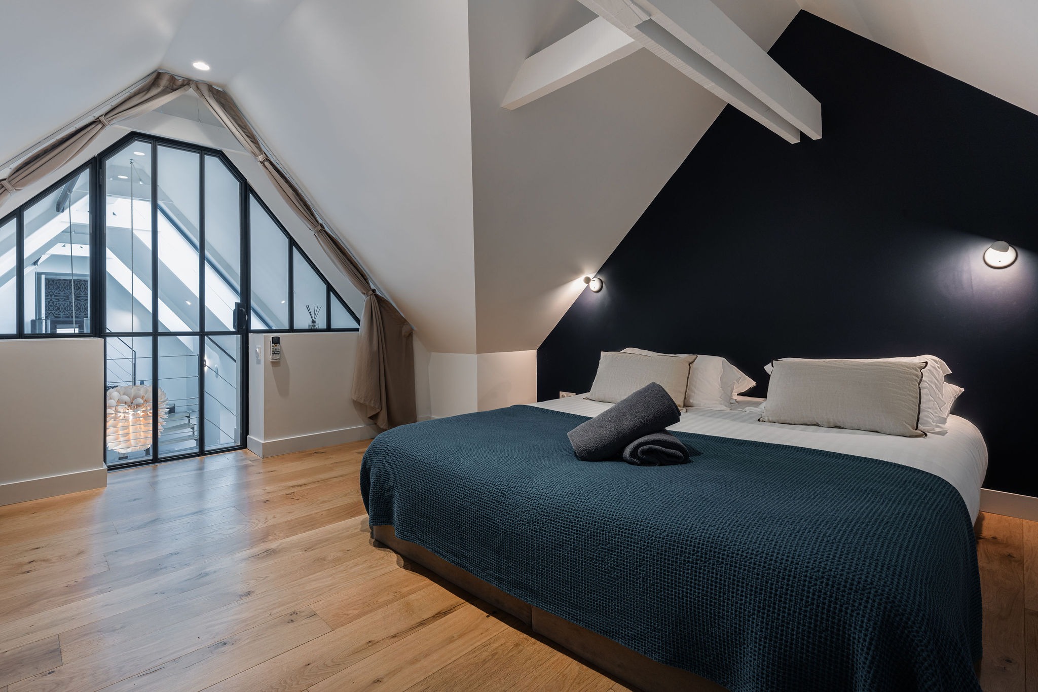 Chambre sous les combles avec grand lit double, mur bleu nuit, verrière intérieure donnant sur le séjour, ambiance cocon