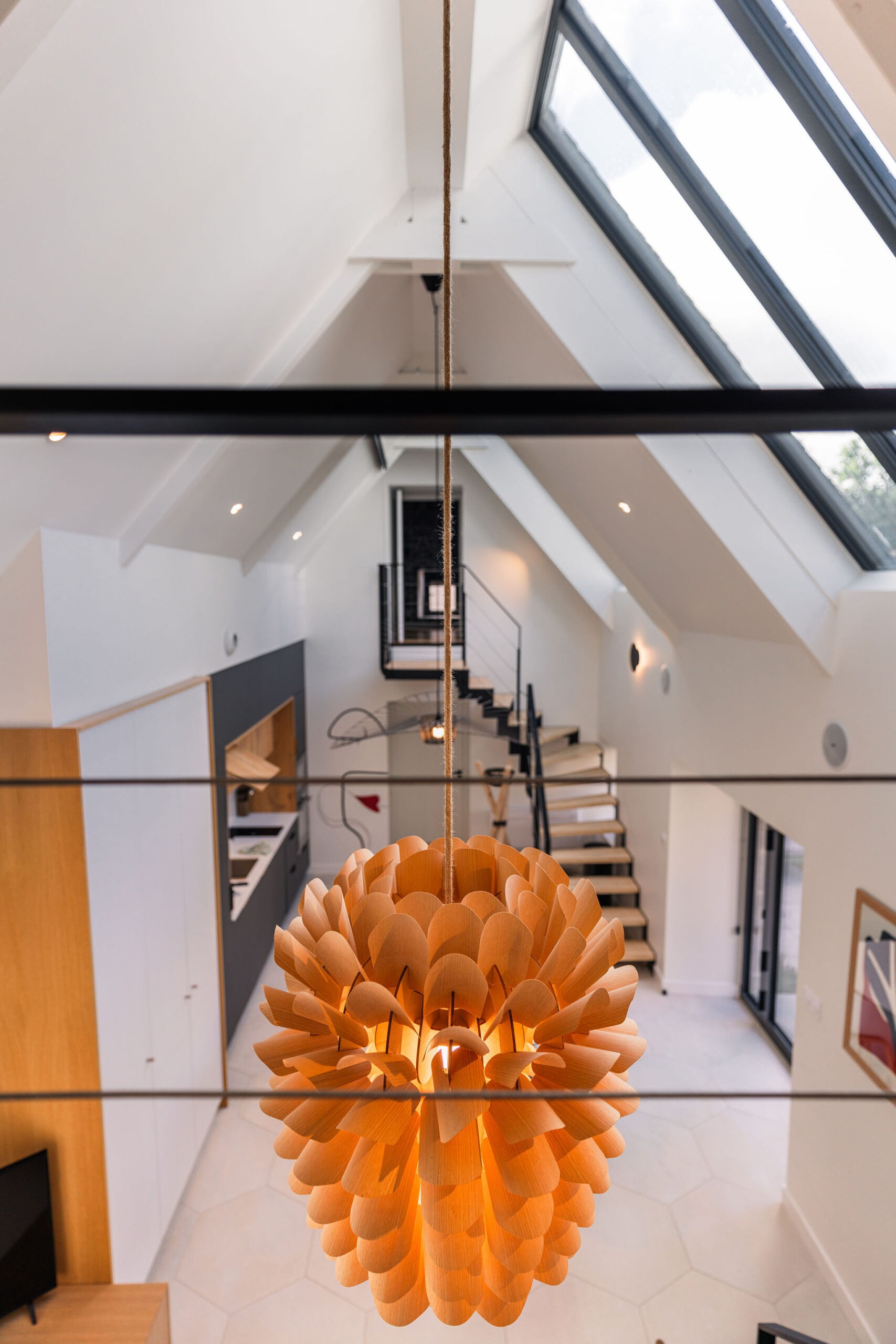Vue plongeante depuis le palier de l’étage sur la pièce de vie du gîte L’Étoile du Roy avec suspension design et verrière