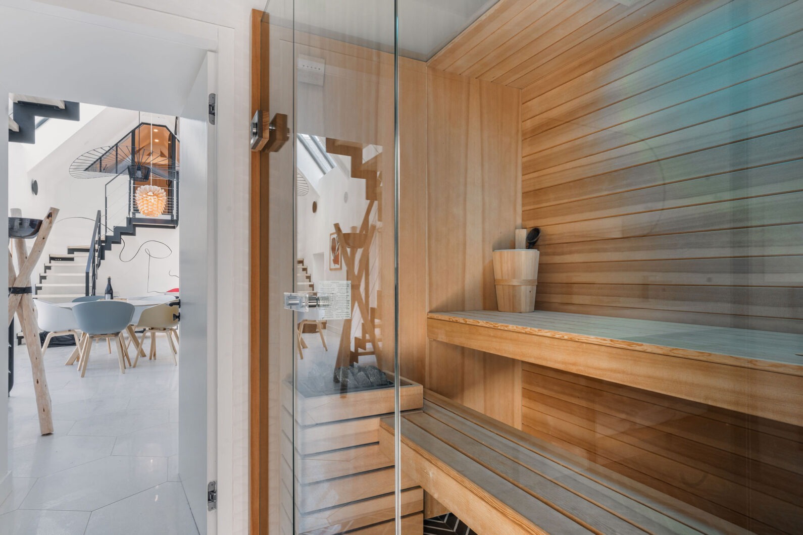 Sauna intérieur en bois clair, traditionnel finlandais, avec porte vitrée et vue sur la salle à manger design en arrière-plan