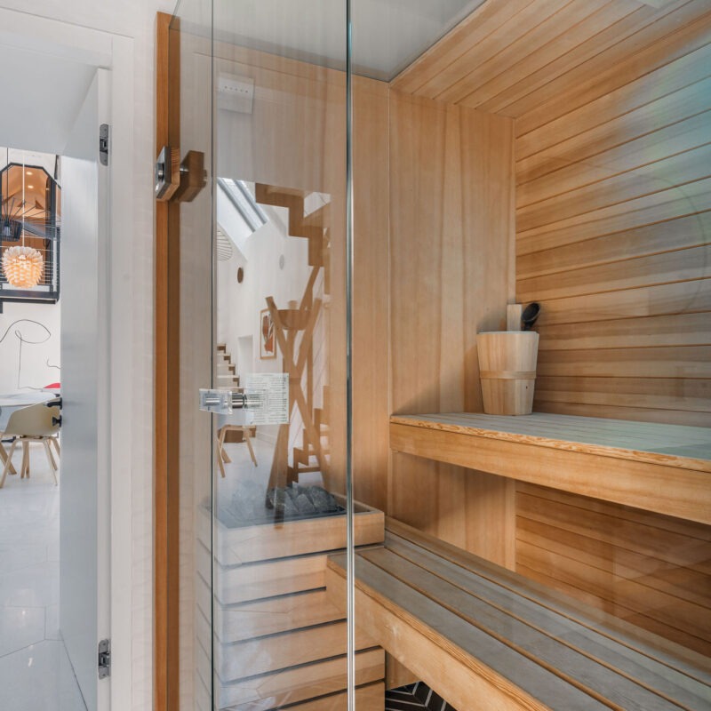 Sauna intérieur en bois clair, traditionnel finlandais, avec porte vitrée et vue sur la salle à manger design en arrière-plan