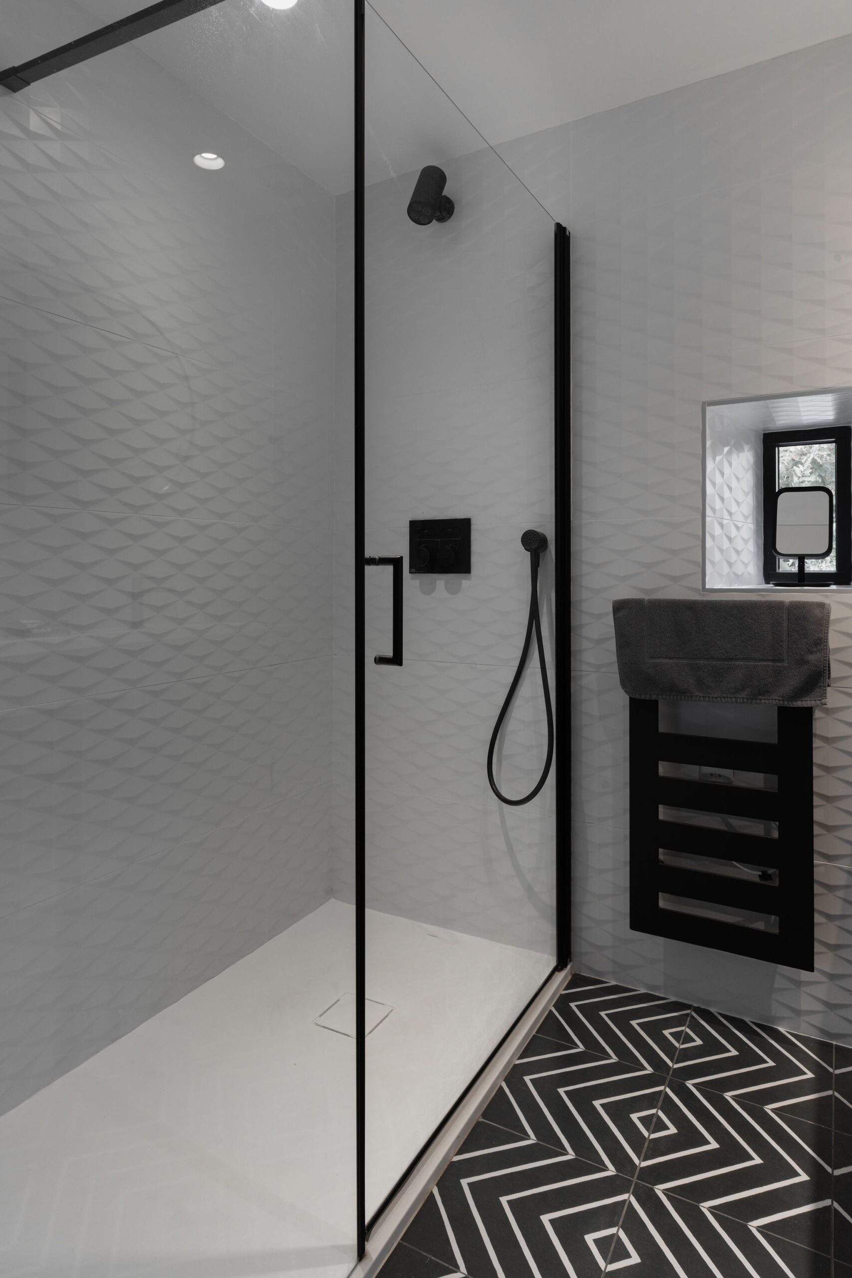 Salle de bain moderne avec douche à l’italienne, carrelage graphique et robinetterie noire dans le logement L'Étoile du Roy au Domaine de Stang Bihan