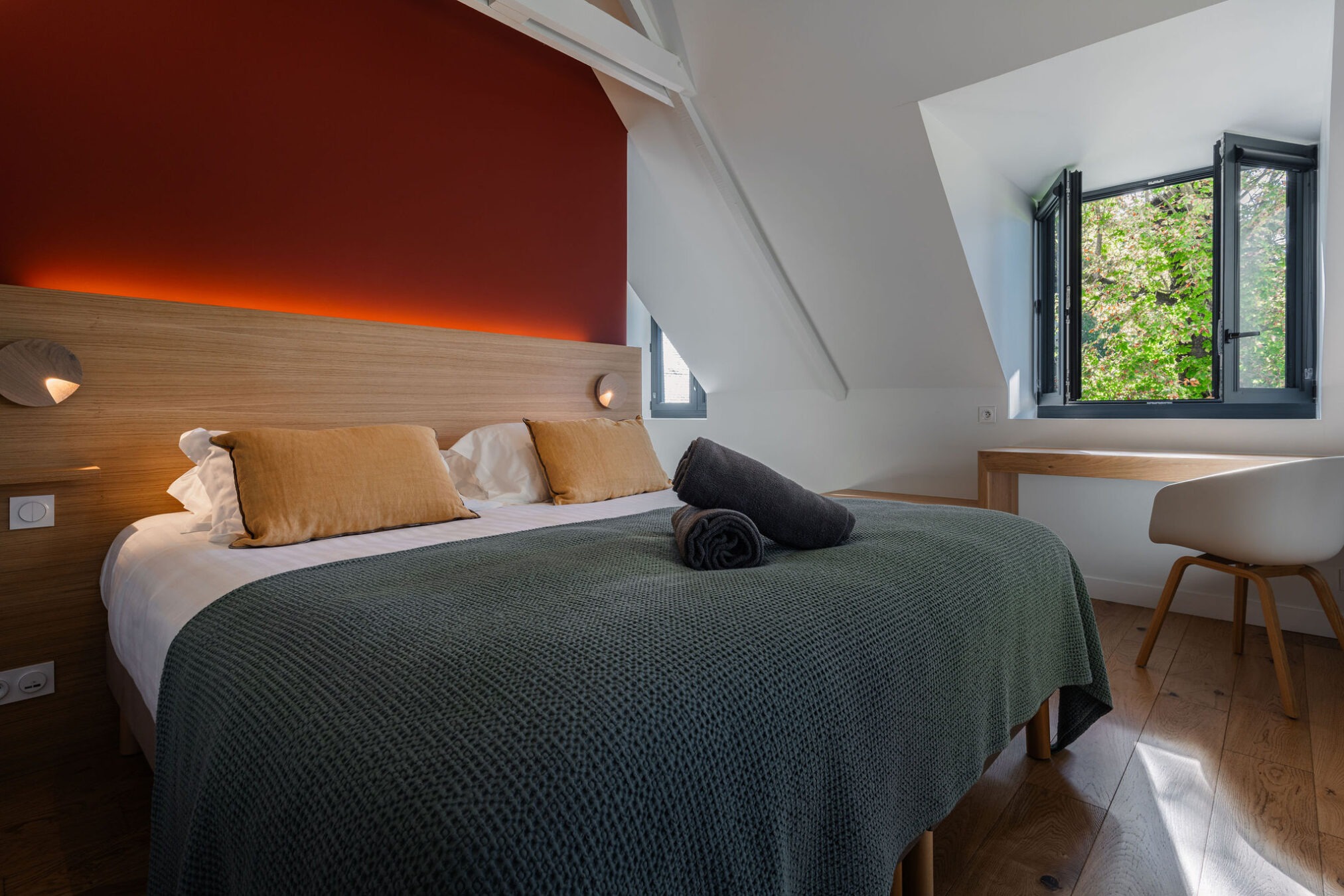 Chambre du logement Belem avec lit double, parure de lit en laine, luminaires modernes et vue sur le parc, au Manoir de Stang Bihan à Concarneau.