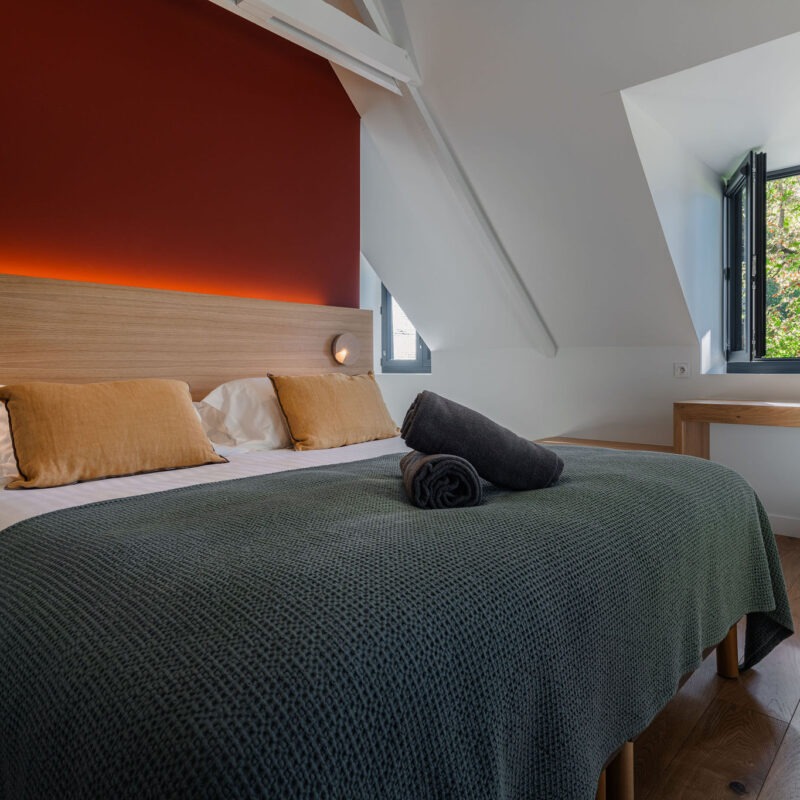 Chambre du logement Belem avec lit double, parure de lit en laine, luminaires modernes et vue sur le parc, au Manoir de Stang Bihan à Concarneau.